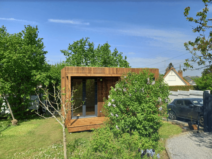 Studio de jardin en bois derrière un petit arbuste